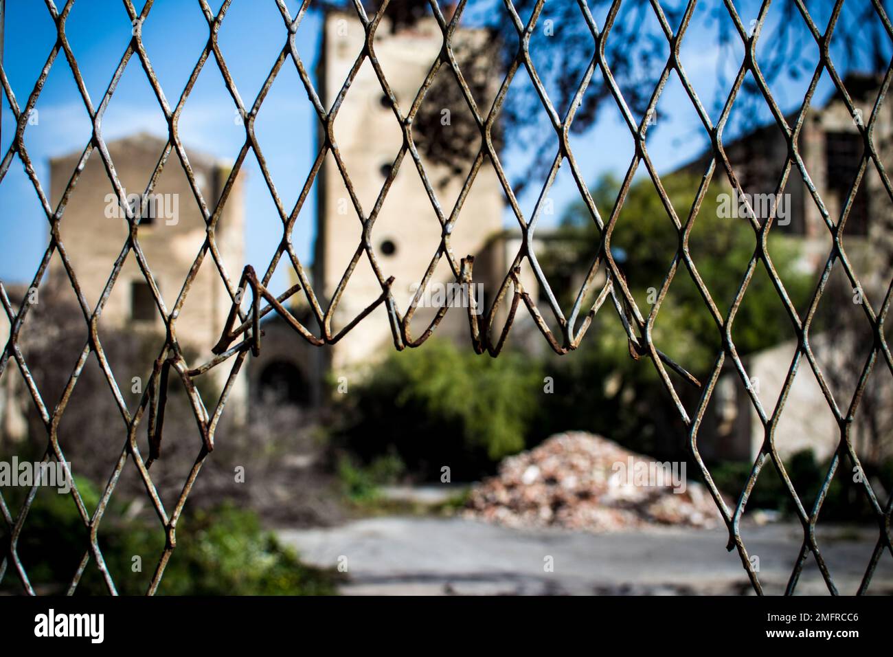 Broken metal fence with old distillery of San Paolo in Noto blurred in the background Stock Photo