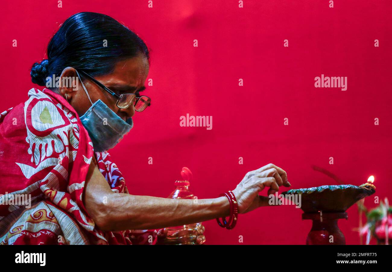 An elderly Indian woman wearing a face mask lights an oil lamp