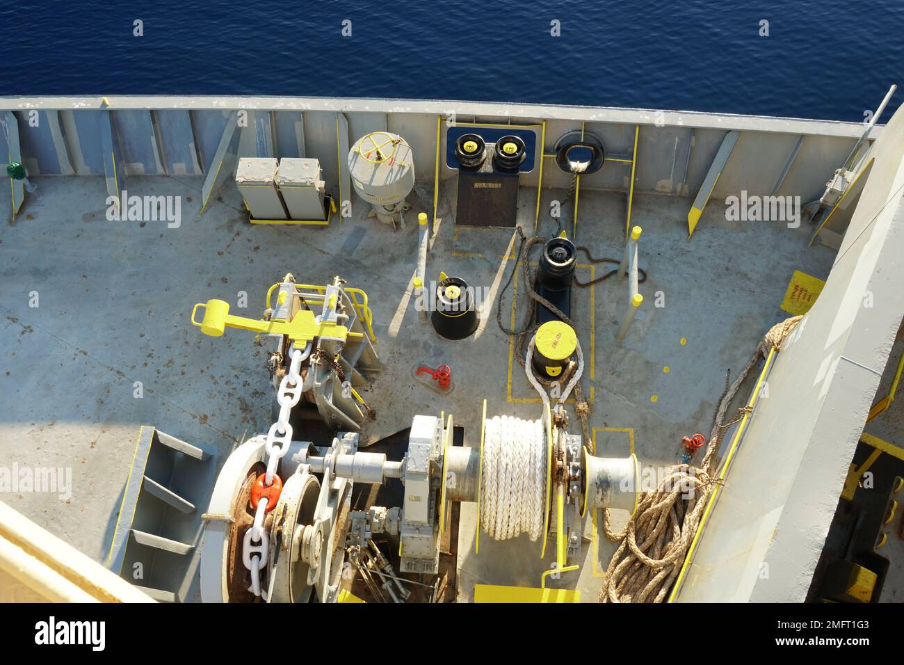 View from top of mast on black and yellow painted bollards, mooring roller and mooring winch with white rope in forward manoeuvring station. Stock Photo