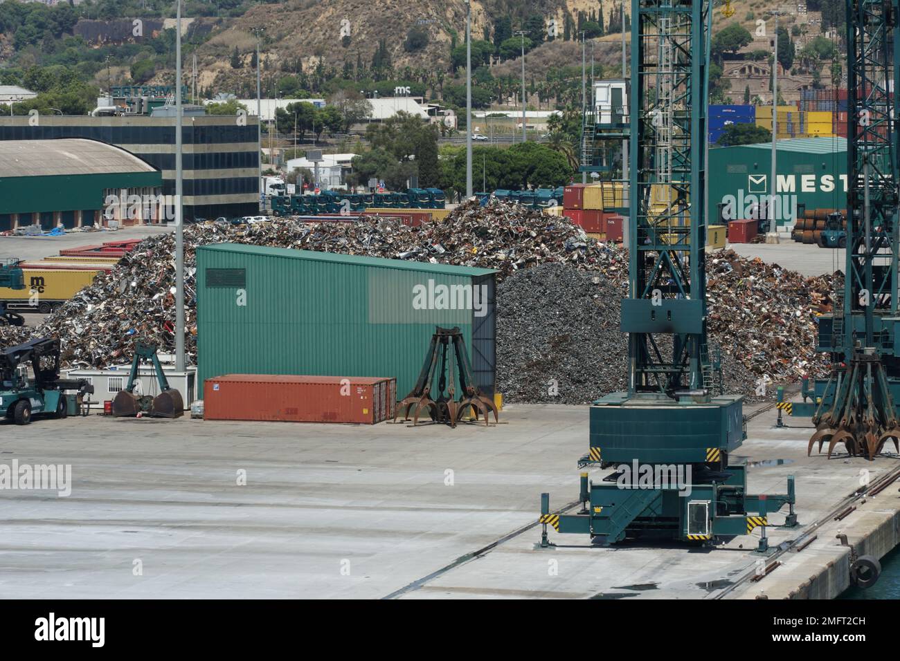 View on heap of metal scrap and green cargo cranes situated in the port ready for loading on the ships. Stock Photo