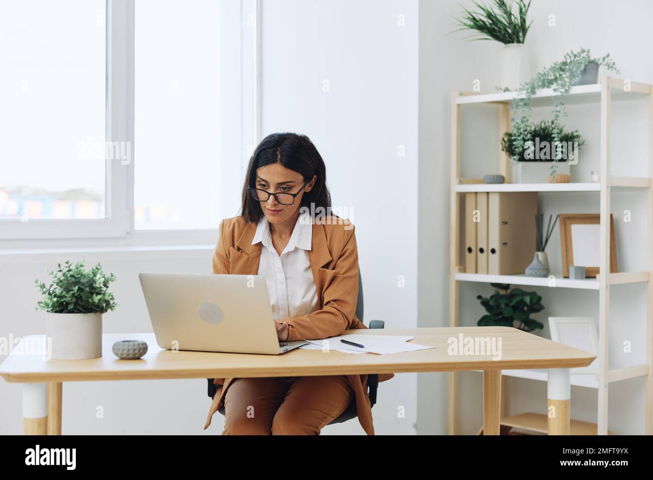 Business woman working in an office at a desk with a laptop in a beige ...