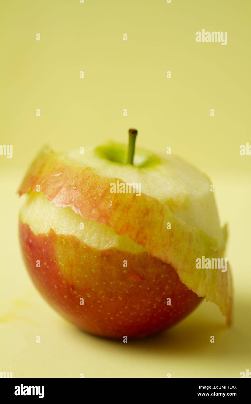 Close up of one Braeburn apple with some of the skin peeled on a plain background Stock Photo