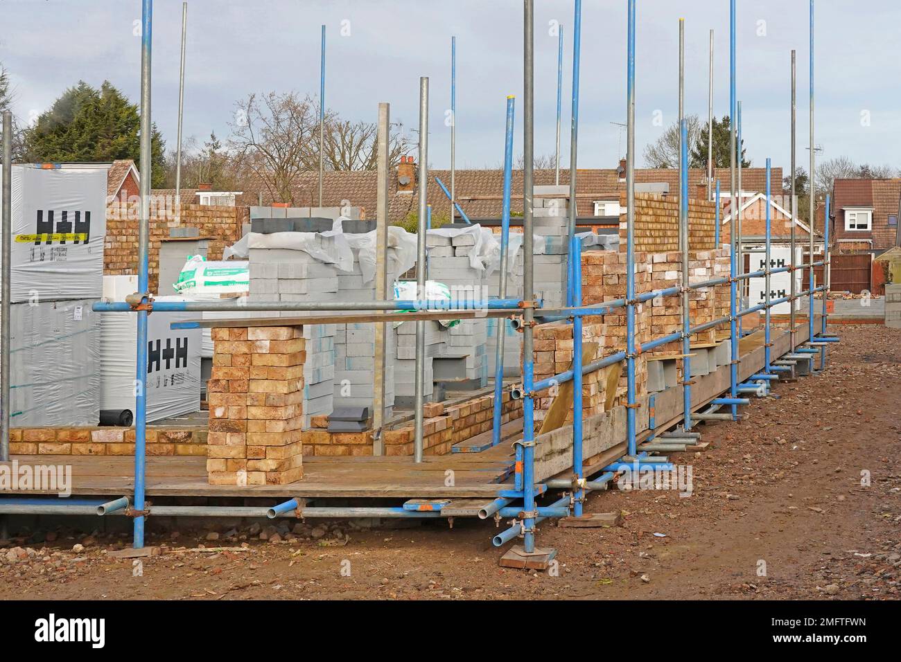 Front corner of new brick and block walls being built for new detached residential property scaffolding erected building materials stacked England UK Stock Photo