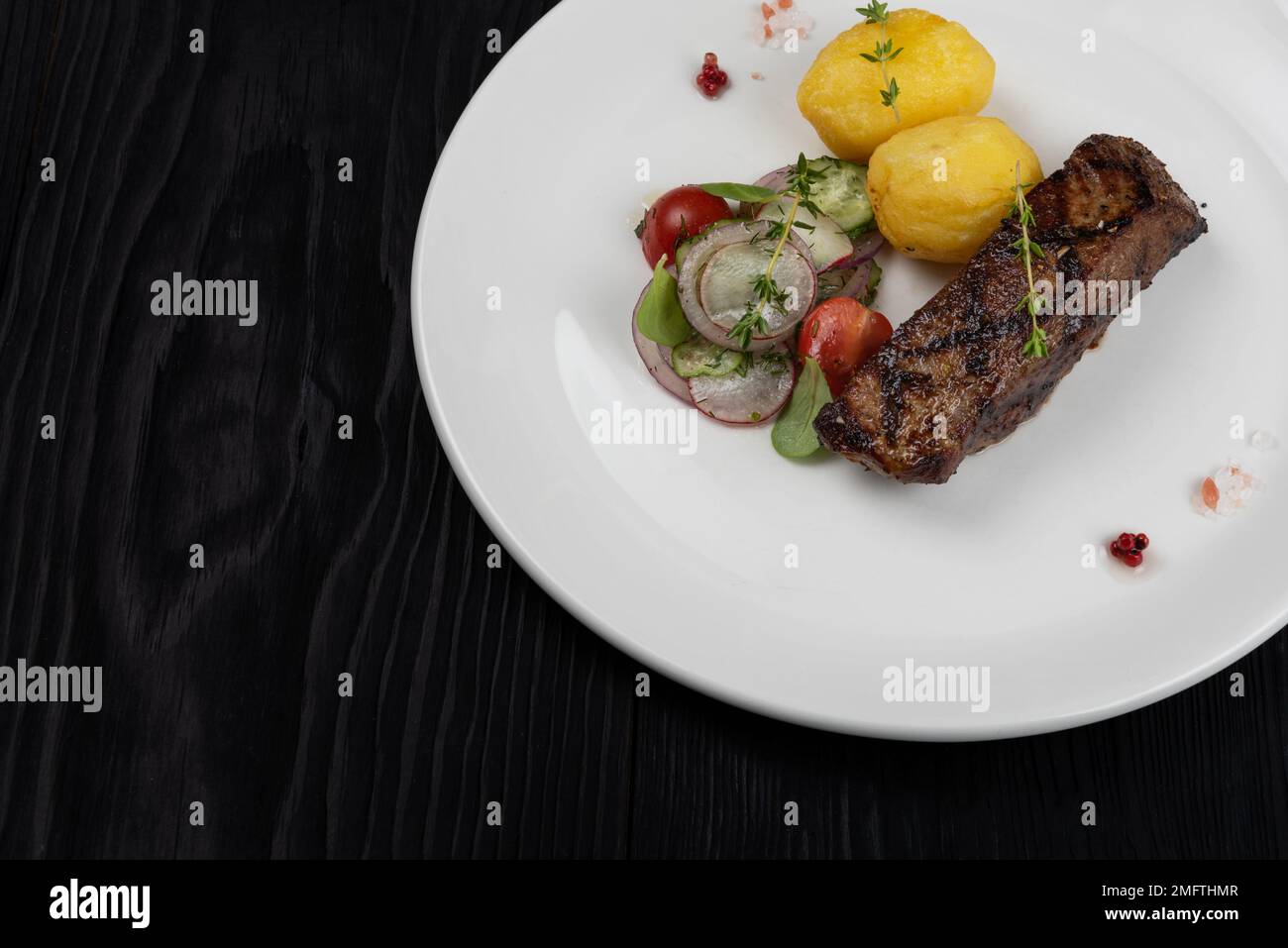 Grilled beef skirt steak meat with potato and vegetables on white plate on wooden black background Stock Photo