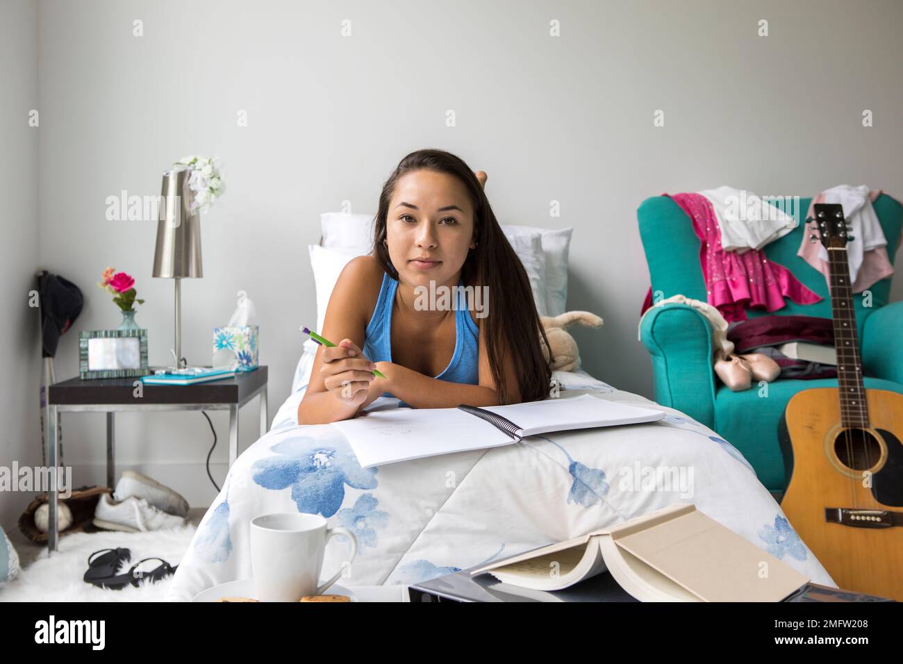 A teenage girl does homework on her bed in her bedroom. Stock Photo
