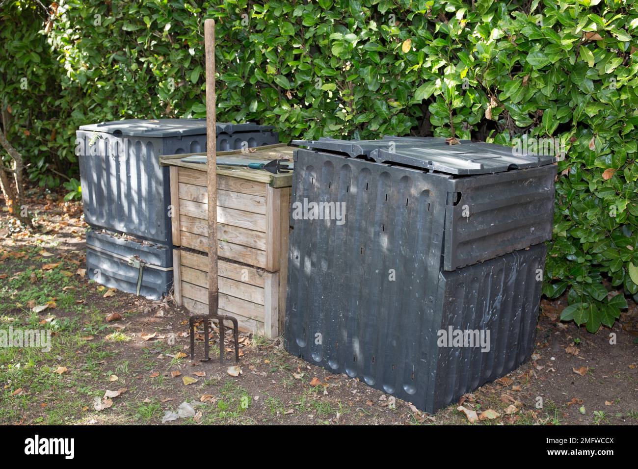 Garden fork turning black composted soil in wooden and plastic compost