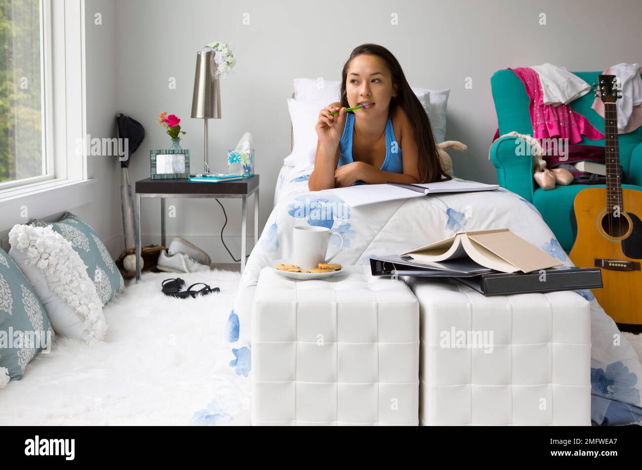 A teenage girl looks pensive in her bedroom as she writes in a notebook. Stock Photo