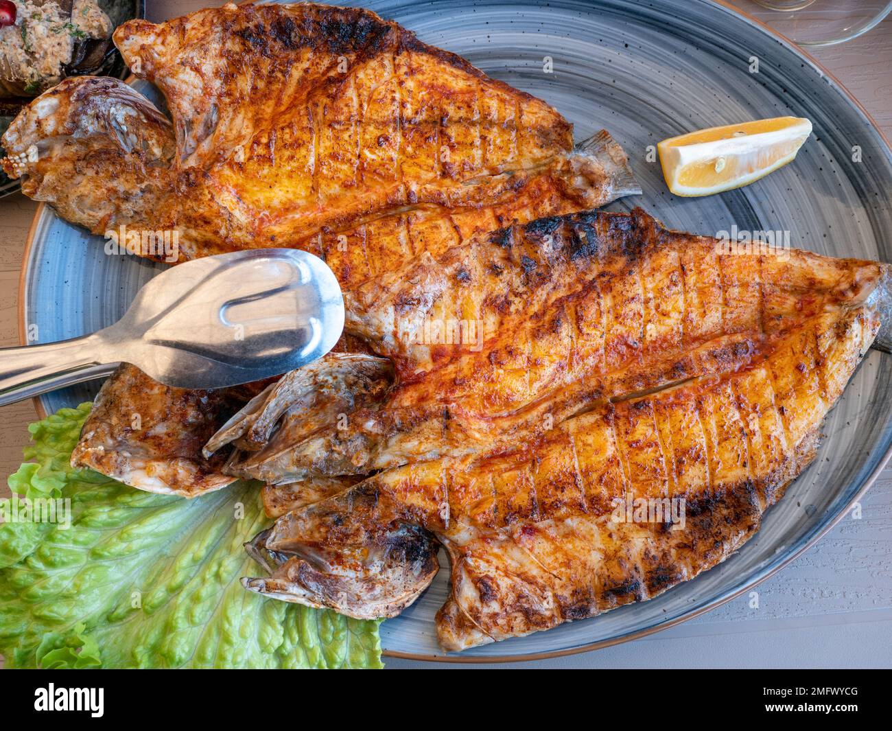 Grilled fish, fried sea bass on plate in restaurant, seafood healthy eating, top view. Stock Photo