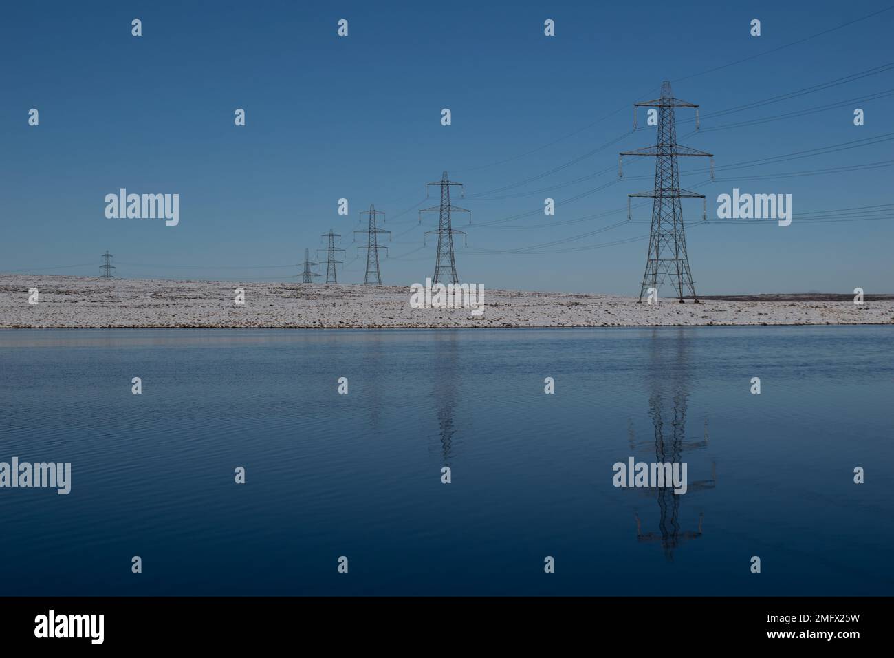 Electricity pylons reflected in water with snow. Copy space Stock Photo