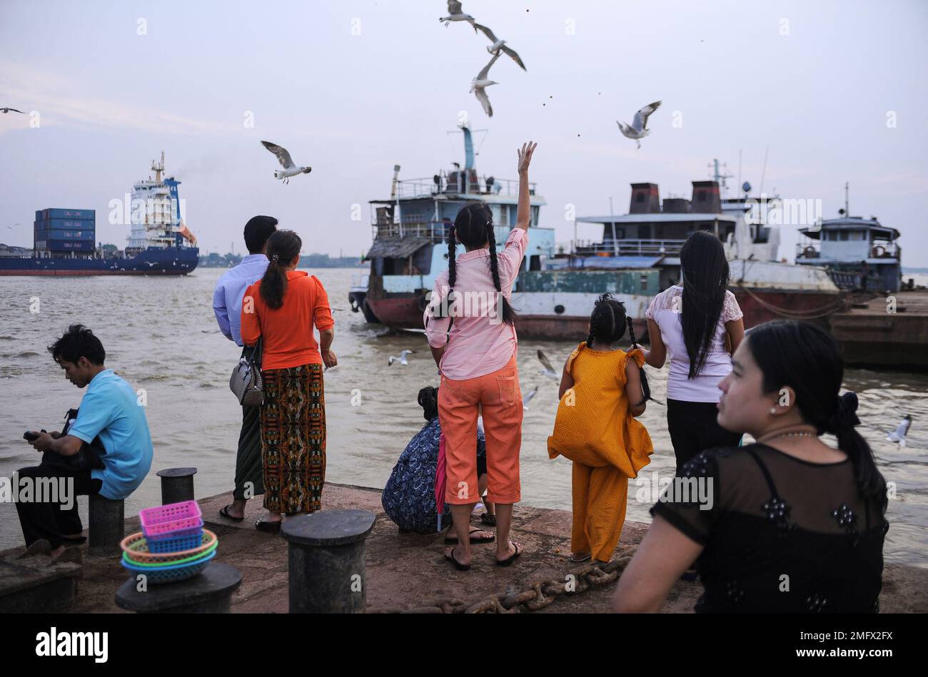 06.05.2014, Yangon, Myanmar, Asia - People feed seagulls from a jetty at the waterfront by the Yangon River (Hlaing River) with ships in the backdrop. Stock Photo