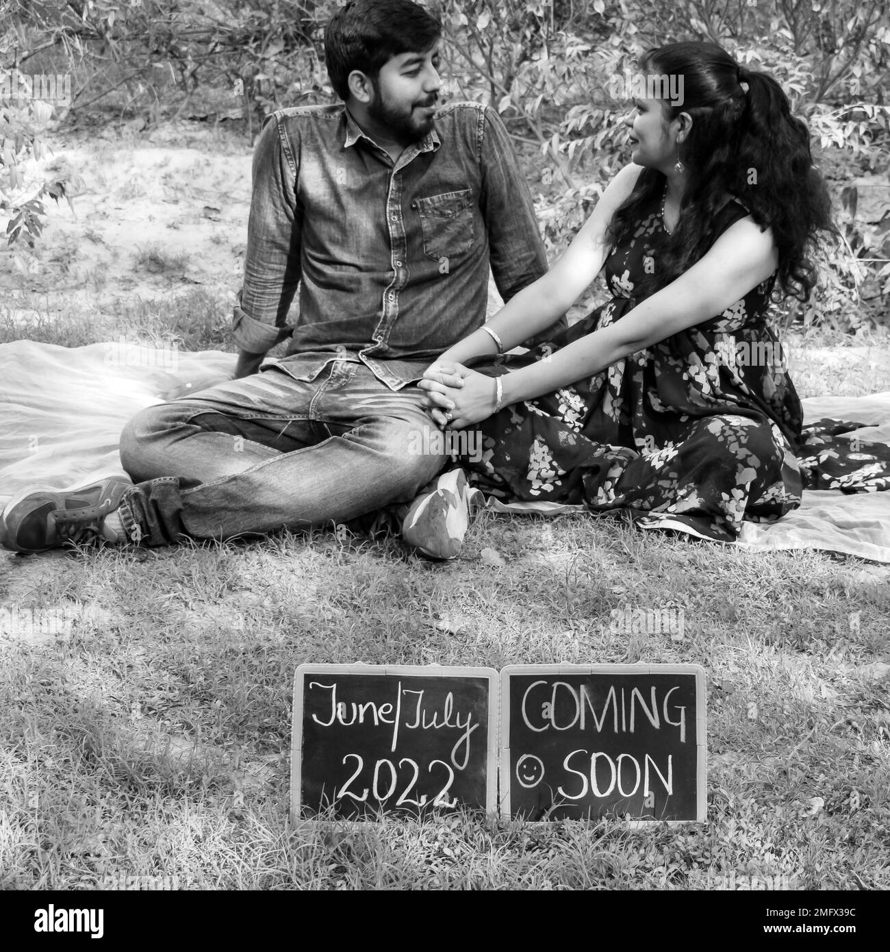 Indian couple posing for maternity baby shoot. The couple is posing in a lawn with green grass and the woman is falunting her baby bump in Lodhi Garde Stock Photo