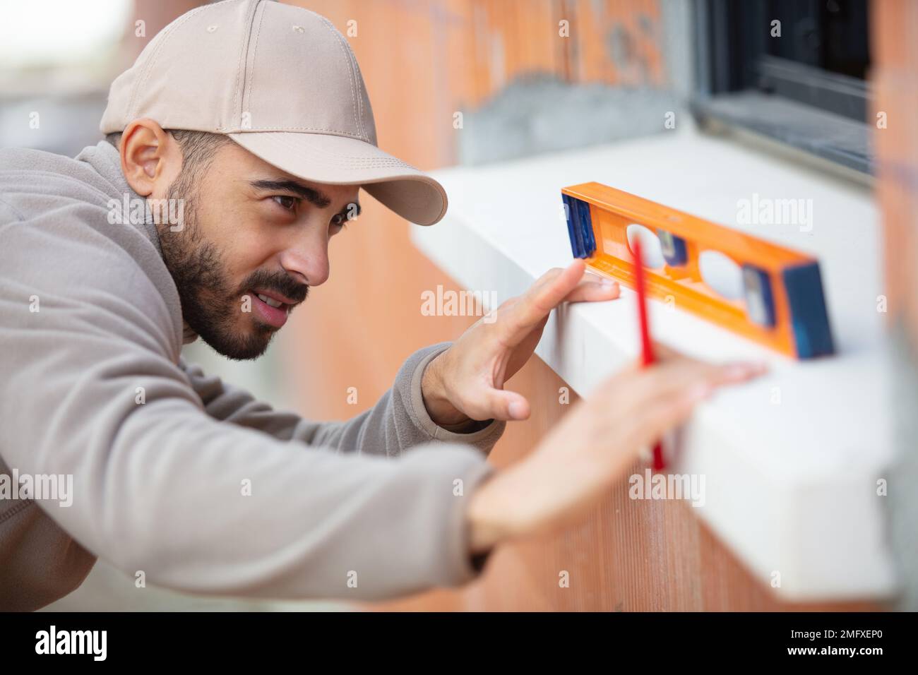 male builder using level tool to measure window outdoors Stock Photo