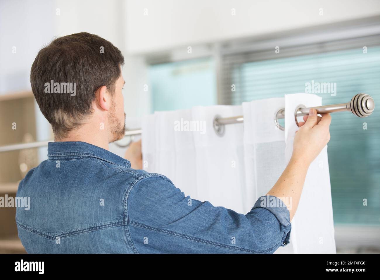 man hanging window curtain indoors interior decor element Stock Photo