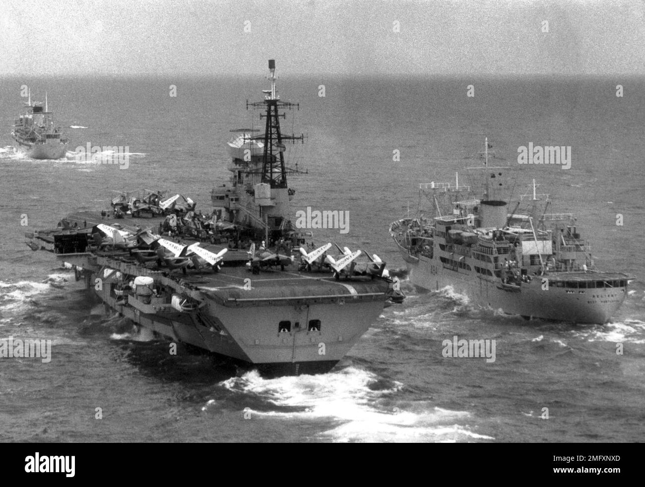Royal Navy warships R31 HMS Warrior a colossus aircraft carrier alongside A84 RFA Reliant an air stores support ship at sea. Stock Photo