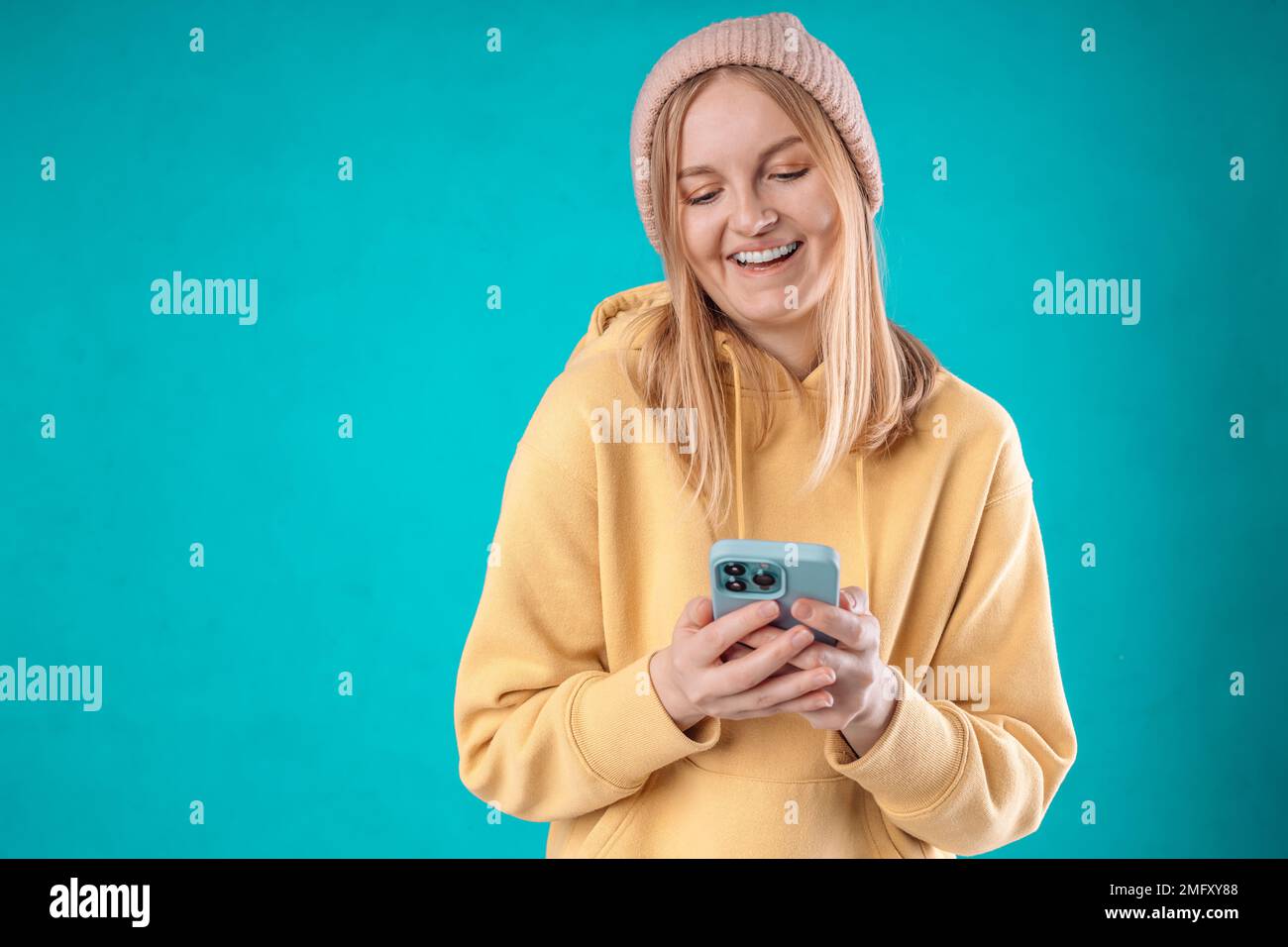 Smiling charming Caucasian woman uses mobile phone happy texting in social networks addicted to modern technologies wears casual jumper isolated over Stock Photo