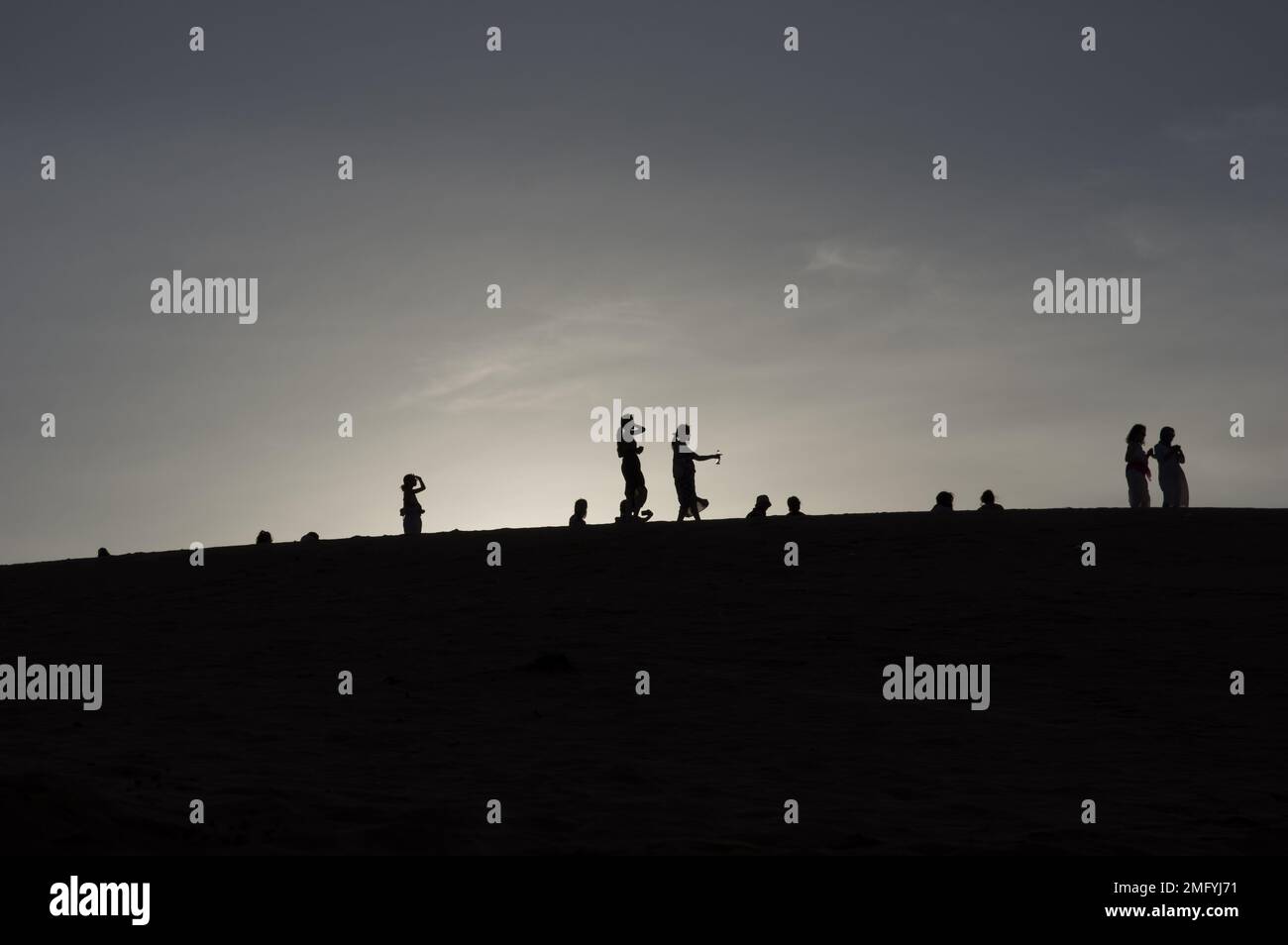 Backlit silhouettes of people on the red sand dunes in Mui Ne Vietnam with the sun setting or rising behind them. Stock Photo