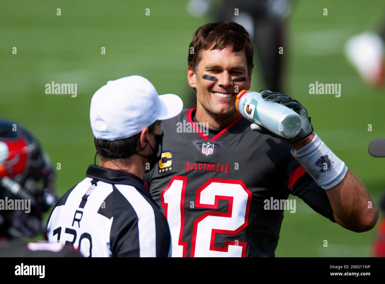 Tampa Bay Buccaneers quarterback Tom Brady (12) drinks from a Gatorade  bottle and smiles at a referee while warming up against the Denver Broncos  before NFL football game, Sunday, Sept.. 27, 2020,