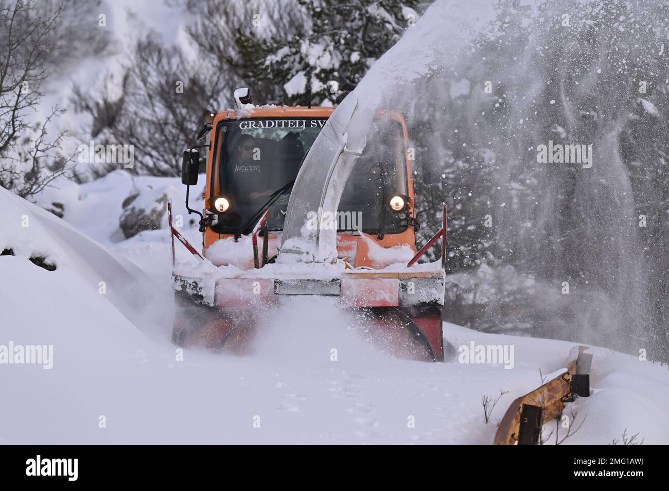 A driver with a snow plow vehicle breaks through the snow-covered road ...