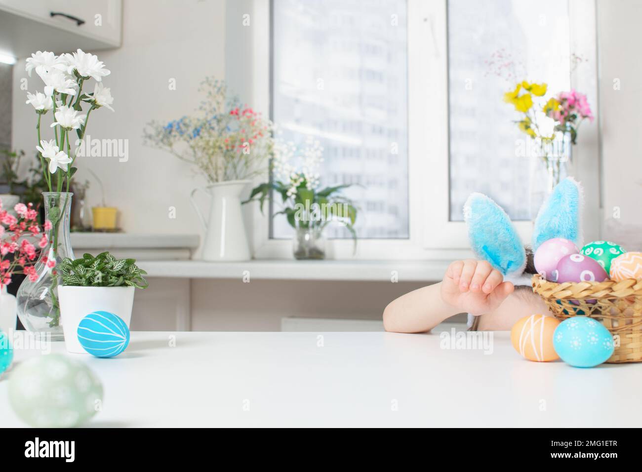 Holiday Easter background with spring flowers, colorful eggs and child's head with bunny ears and empty table Stock Photo