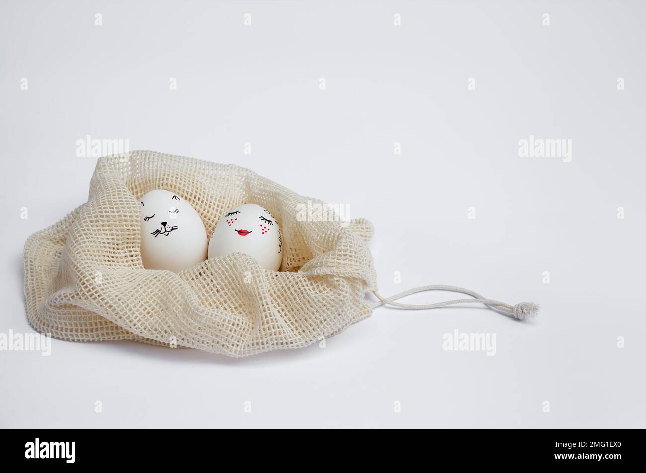 Beautifully painted Easter eggs lie in eco-friendly drawstring mesh bag on white table. Funny spades painted on eggs. Copy space. Happy holidays Stock Photo