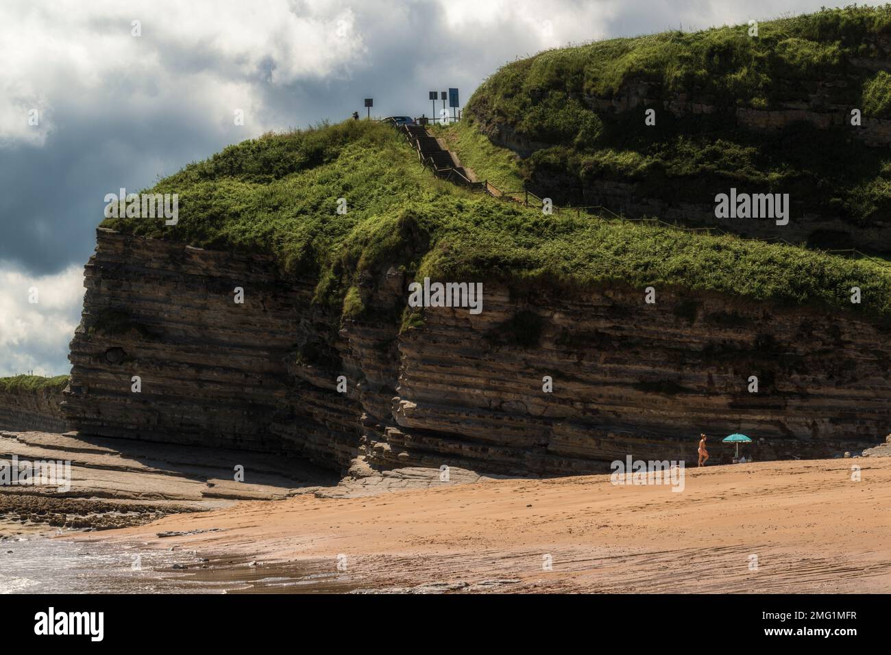 a woman in a thong sunbathing standing next to an umbrella on the cliff of Langre beach, Cantabria, Spain, Europe Stock Photo