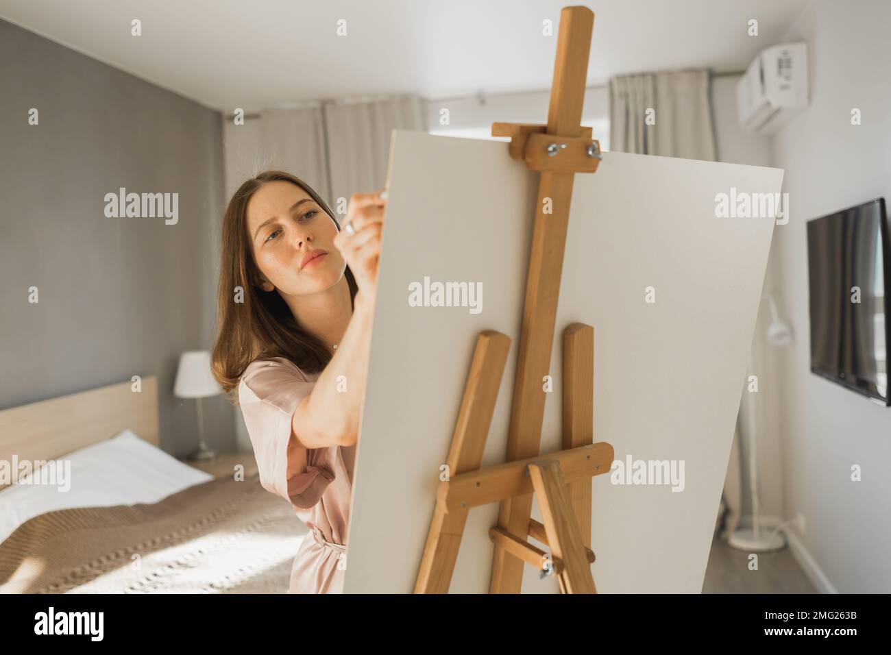 Young woman artist painting on canvas on the easel at home in bedroom ...