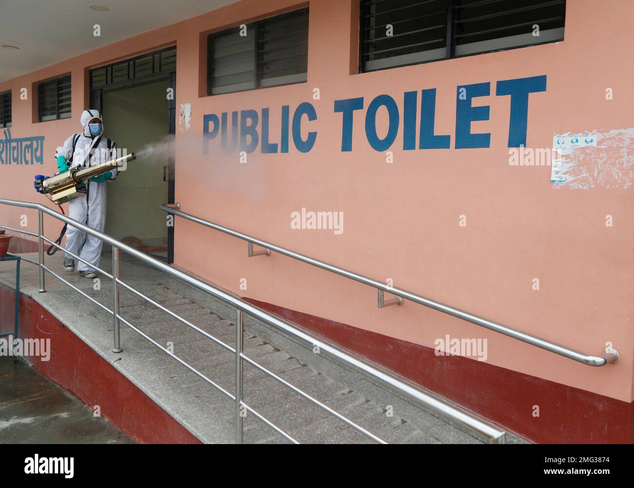 A Nepalese man wearing protective gear disinfects a public toilet at a