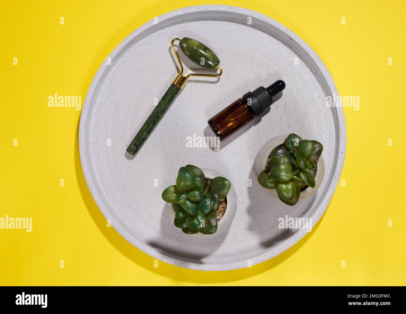 Hand held face massager and brown glass bottle with pipette on round ...