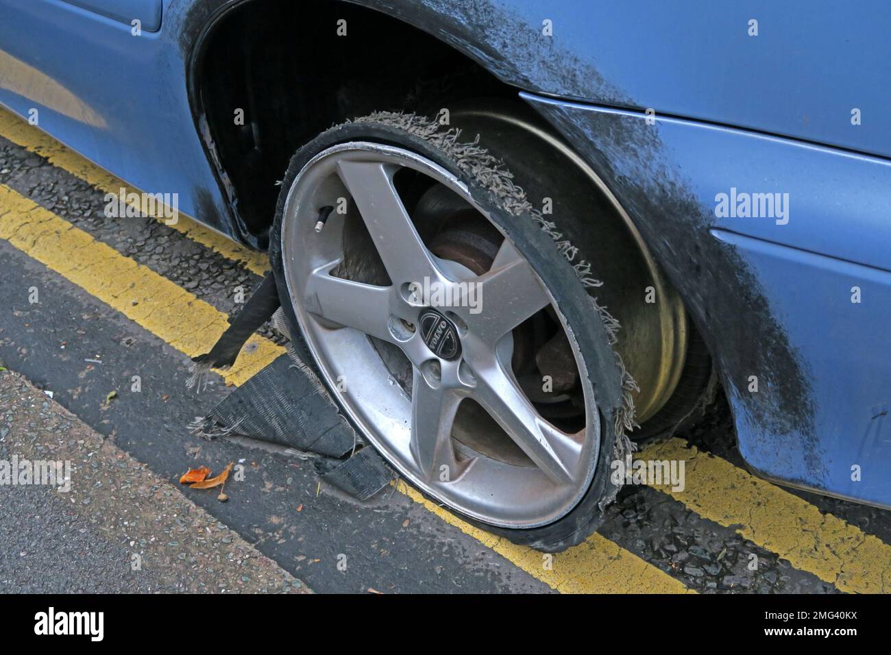 Front car tyre shredded at speed, stopped on double yellow lines, Cheshire, England, UK - Flat low profile tyre on alloy rim, ripped open Stock Photo