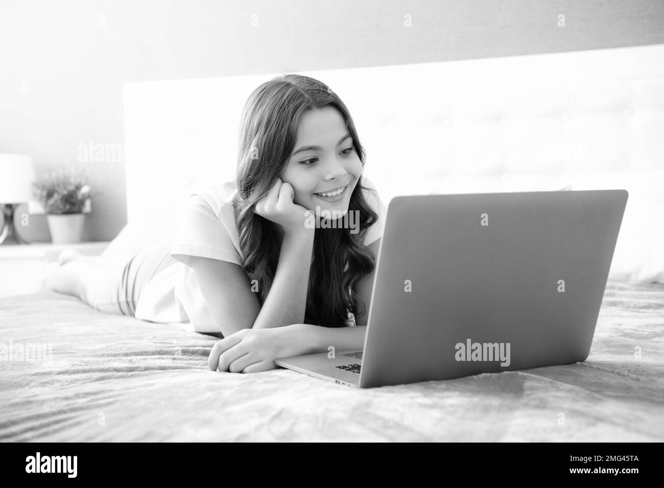 Teen school girl studying at home on bed with laptop. Stock Photo