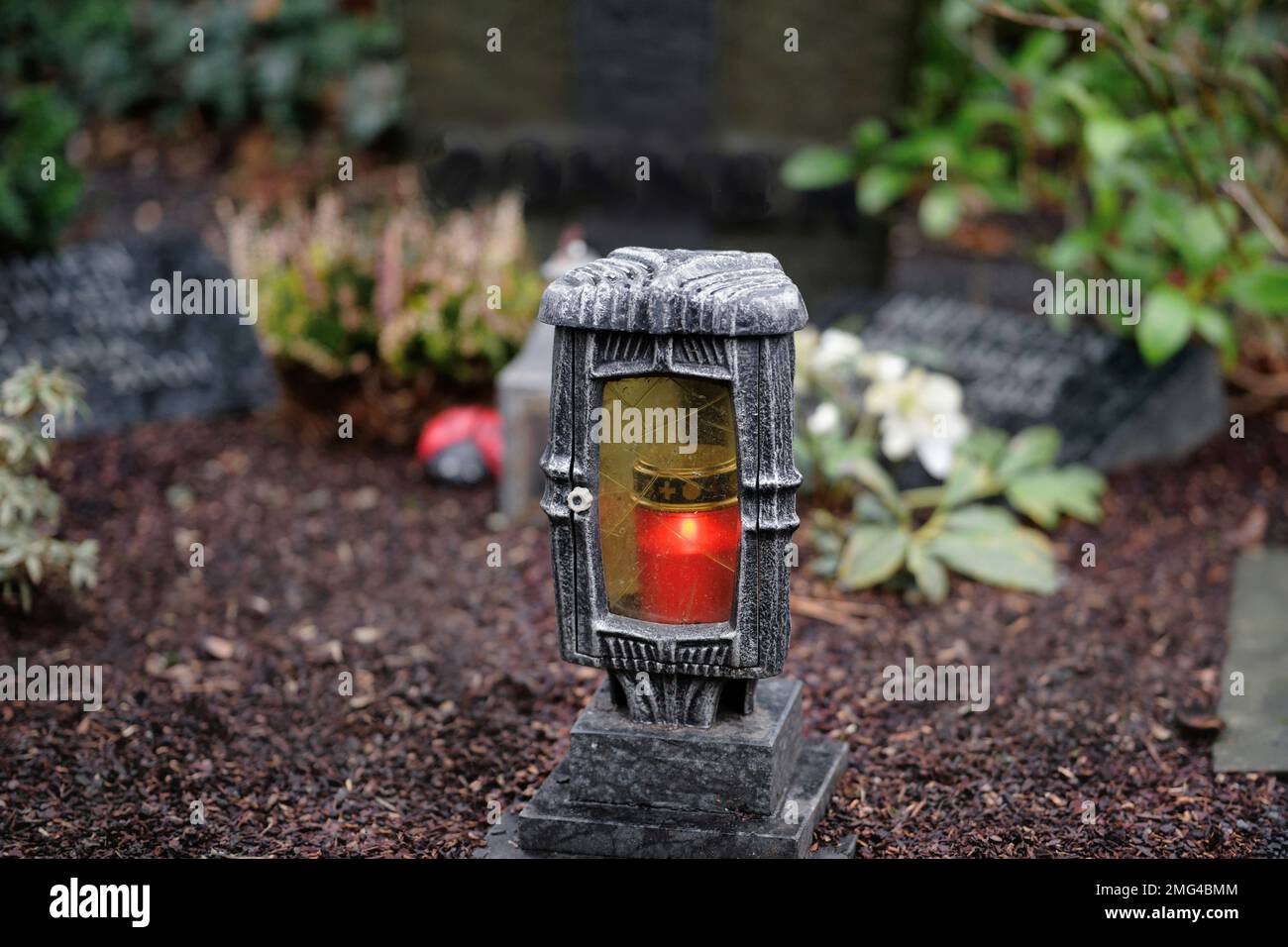 grave lantern with burning red candle and gravestones in blurred background at a cemetery Stock Photo