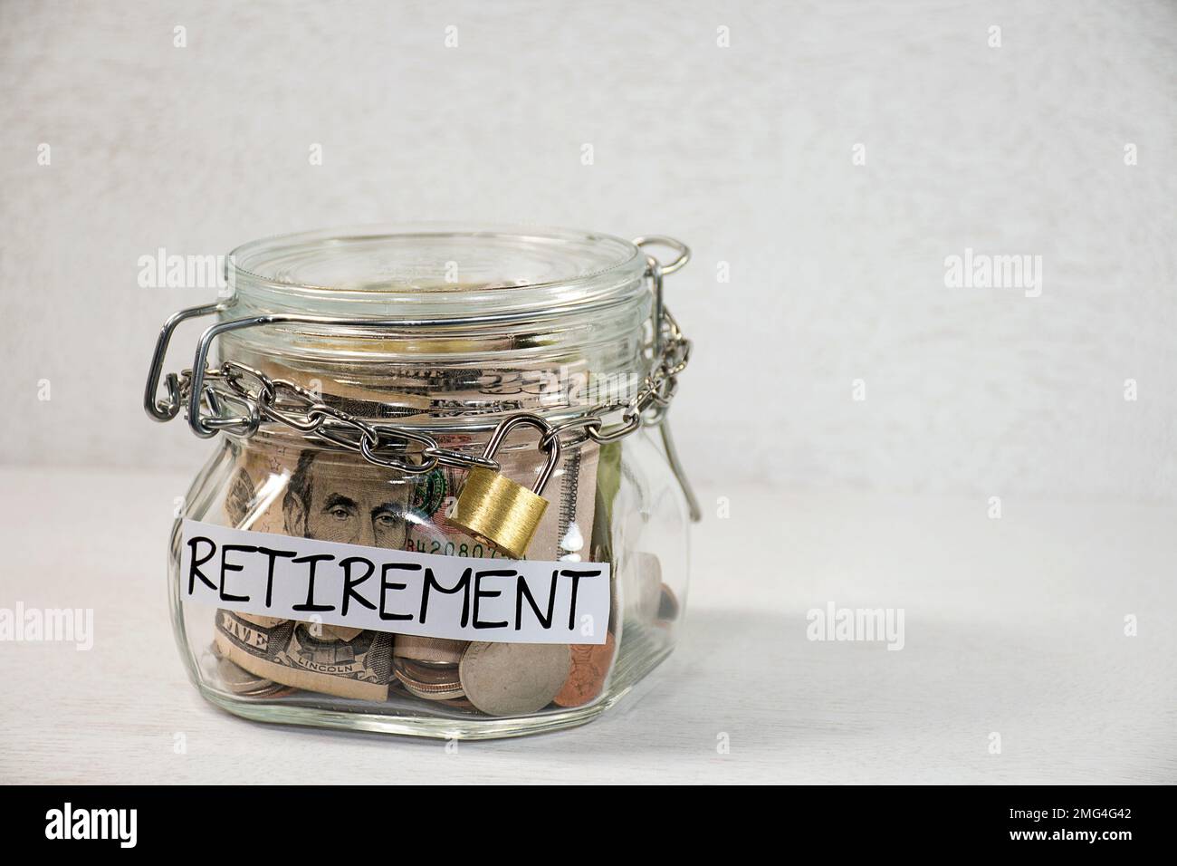 Coins and dollars in a glass retirement jar with a metal chain and padlock Stock Photo