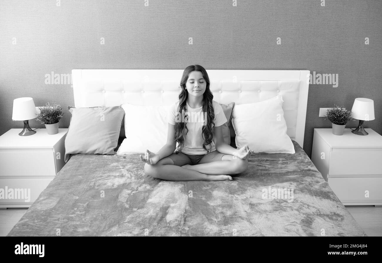 Morning Meditation on bed. Teenager child practicing meditation at bedroom. Relaxed girl on bed in lotus pose and meditating. Stock Photo