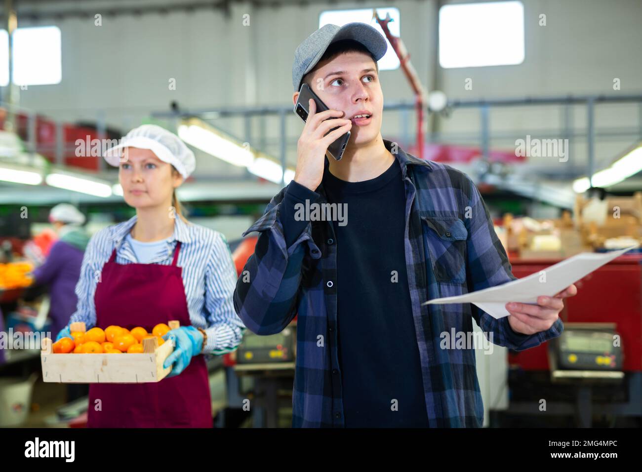 Young supervisor with papers talking on phone in citrus sorting factory Stock Photo