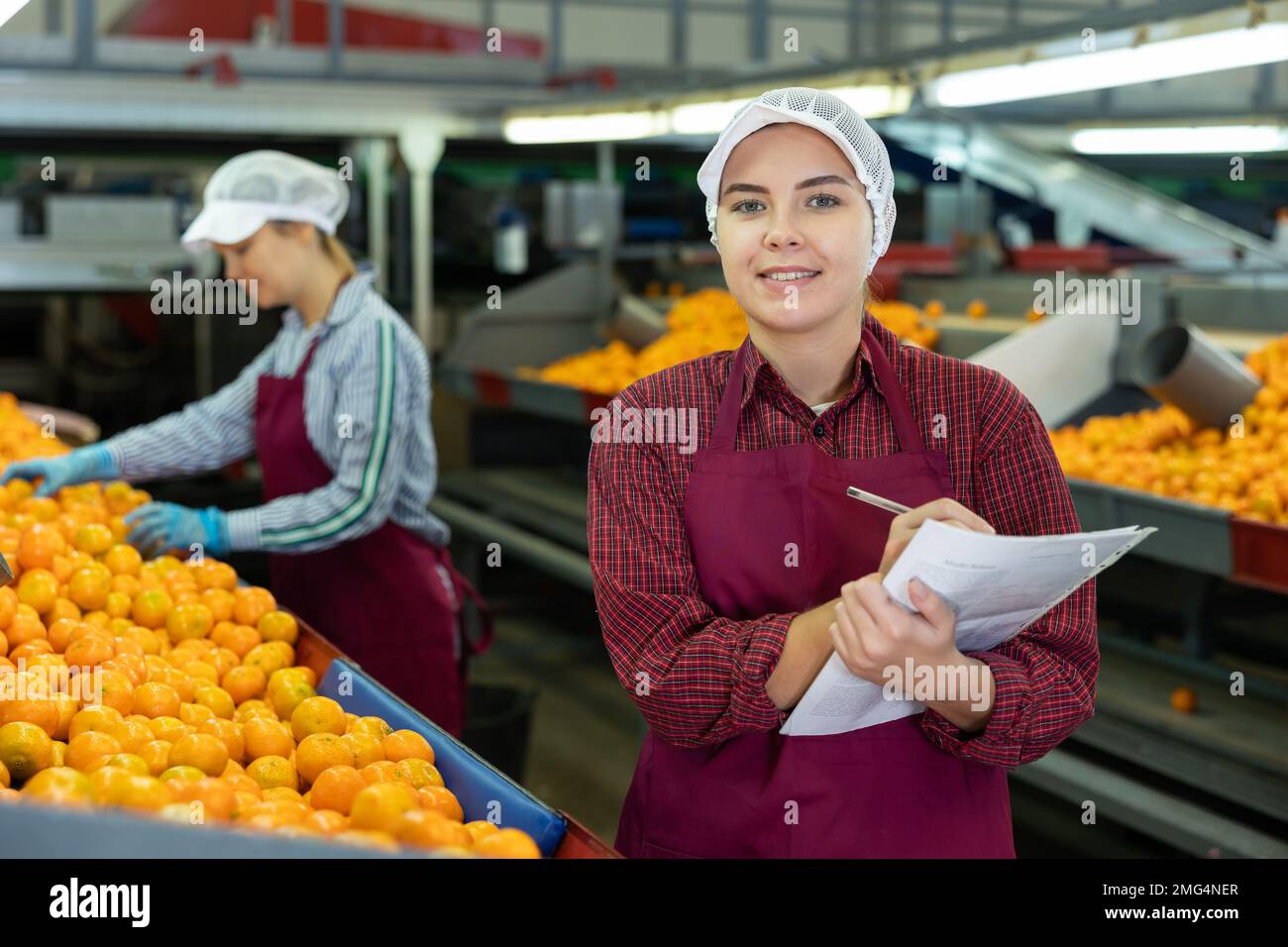 Smiling female shift supervisor with papers at tangerine sorting line Stock Photo