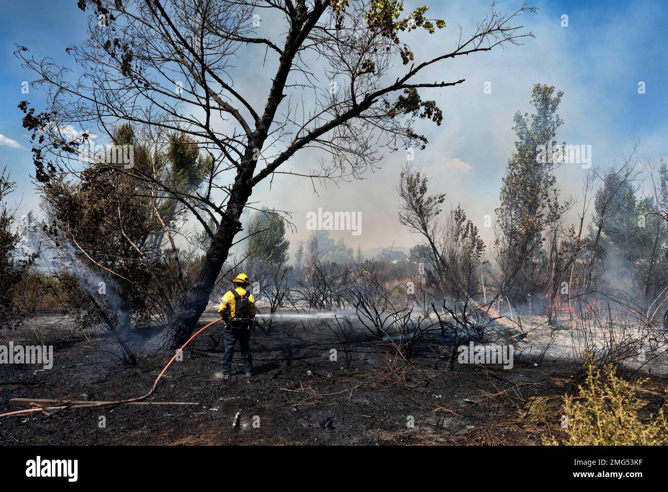 Los Angeles fire department firefighter works to douse the remains of a ...