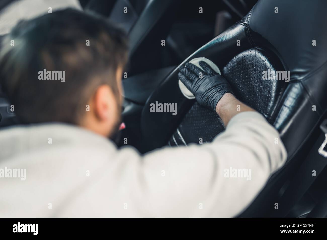 Rear view of man wearing black gloves waterproofing car seat leather