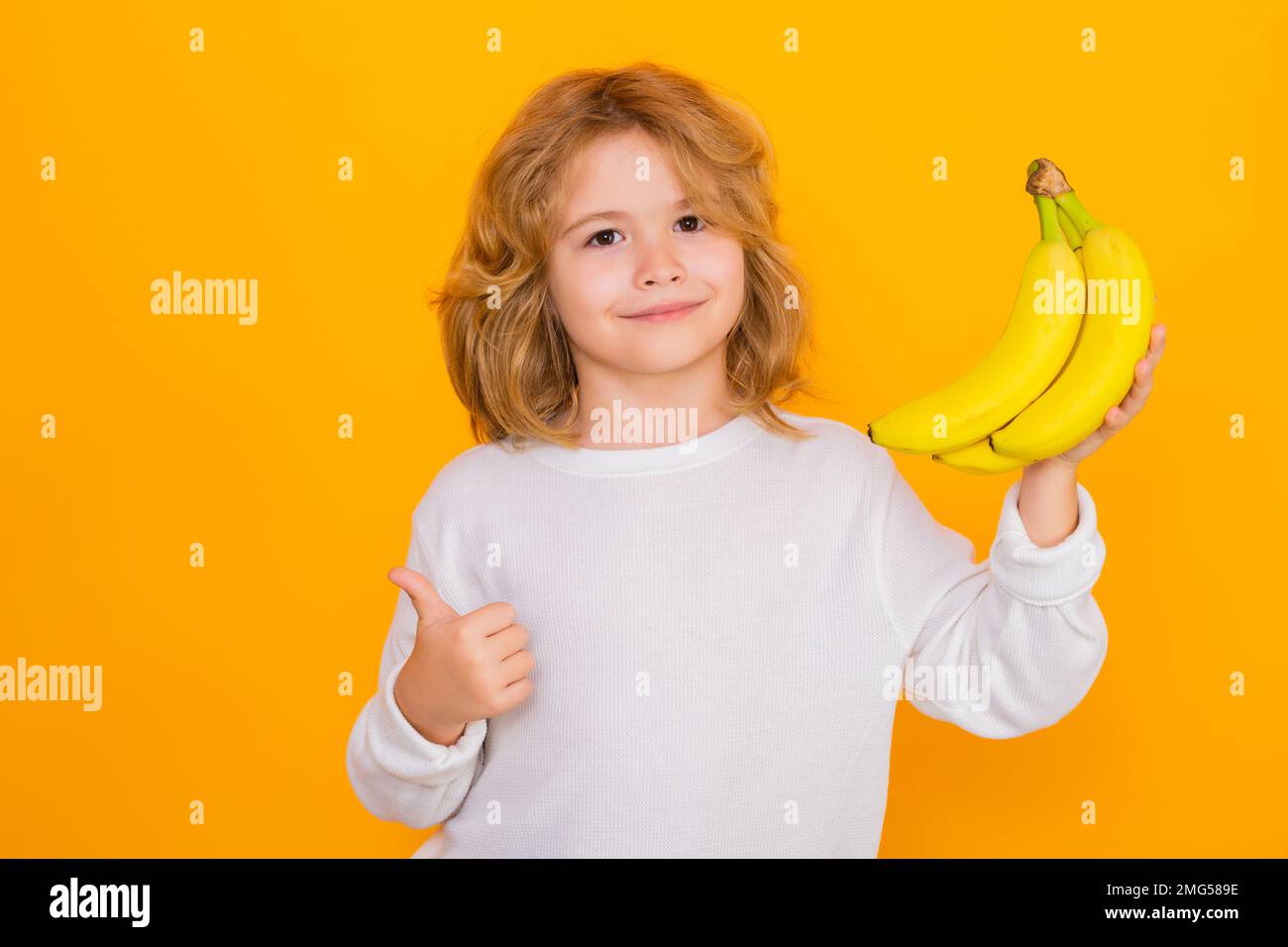 Child hold banana in studio. Studio portrait of cute kid boy with bananas isolated on yellow. Stock Photo