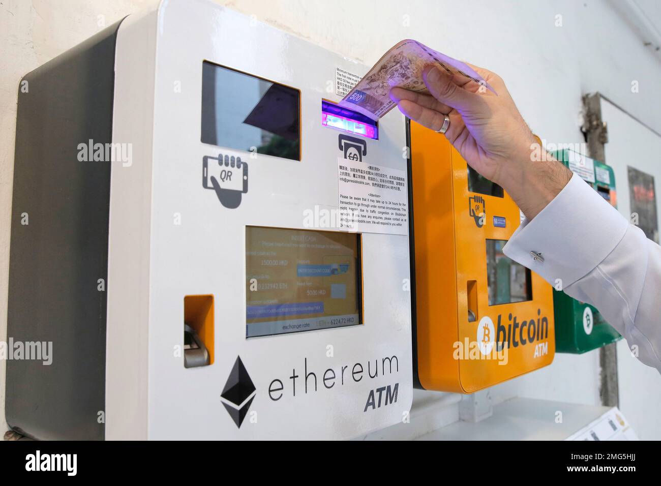 FILE - In this Friday, May 11, 2018 file photo, a man uses an Ethereum ATM  next to a bitcoin ATM, in Hong Kong. A Swiss region that has billed itself  as