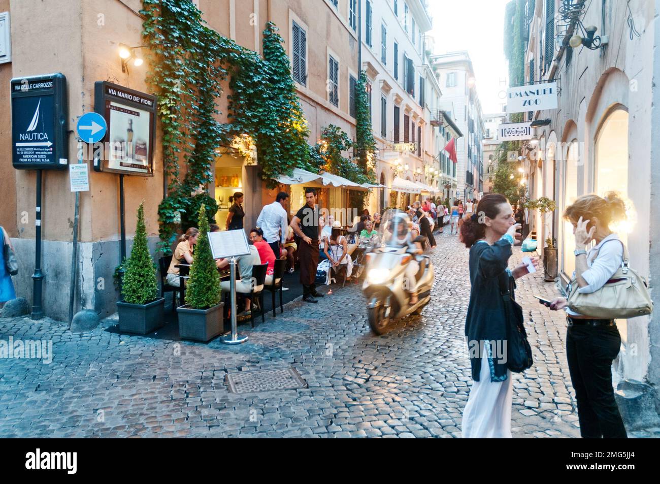 A Rome street scene with diners at outdoor tables and two women chatting to each other Stock Photo