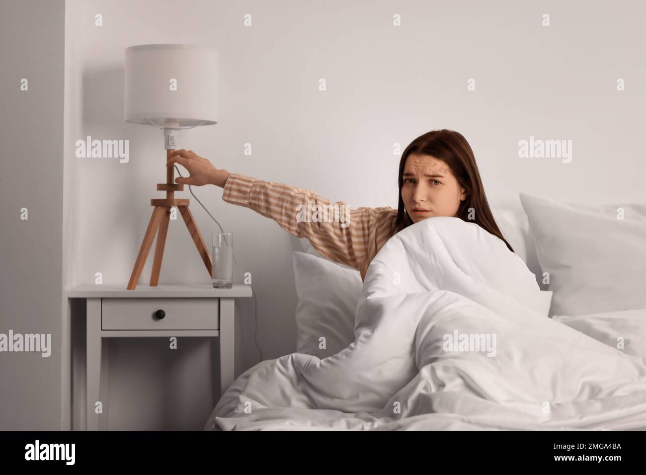 Upset young woman turning on lamp in bedroom Stock Photo