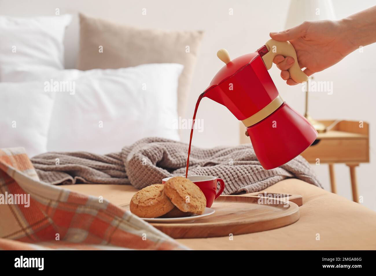 Woman pouring espresso from geyser coffee maker into cup on bed Stock Photo