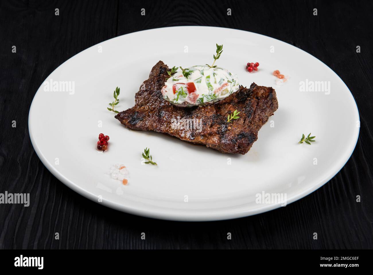 Grilled skirt beef meat steak on a plate with white vegetable sauce decorated by herbs and berries. Dark wooden background Stock Photo