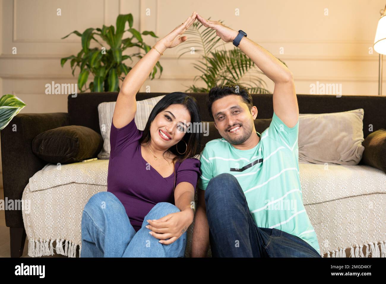happy smiling couple showing by making home roof gesture by joining hands while looking at camera at there new home or apartment - concept of new home Stock Photo