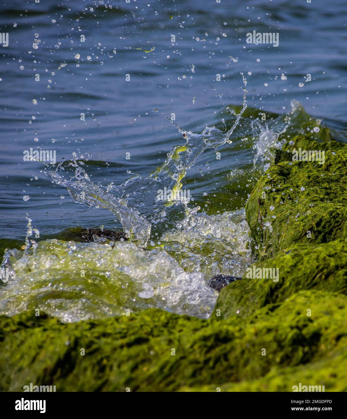 Sea waves crash against large rocks on the shore, forming large splashes.. Stock Photo