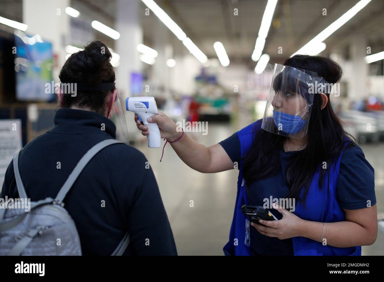 Sam's Club employee Alondra Gonzalez takes the temperature of a customer  entering the store, inside Patio Santa Fe shopping mall where businesses  deemed essential have been operating with health and safety protocols,
