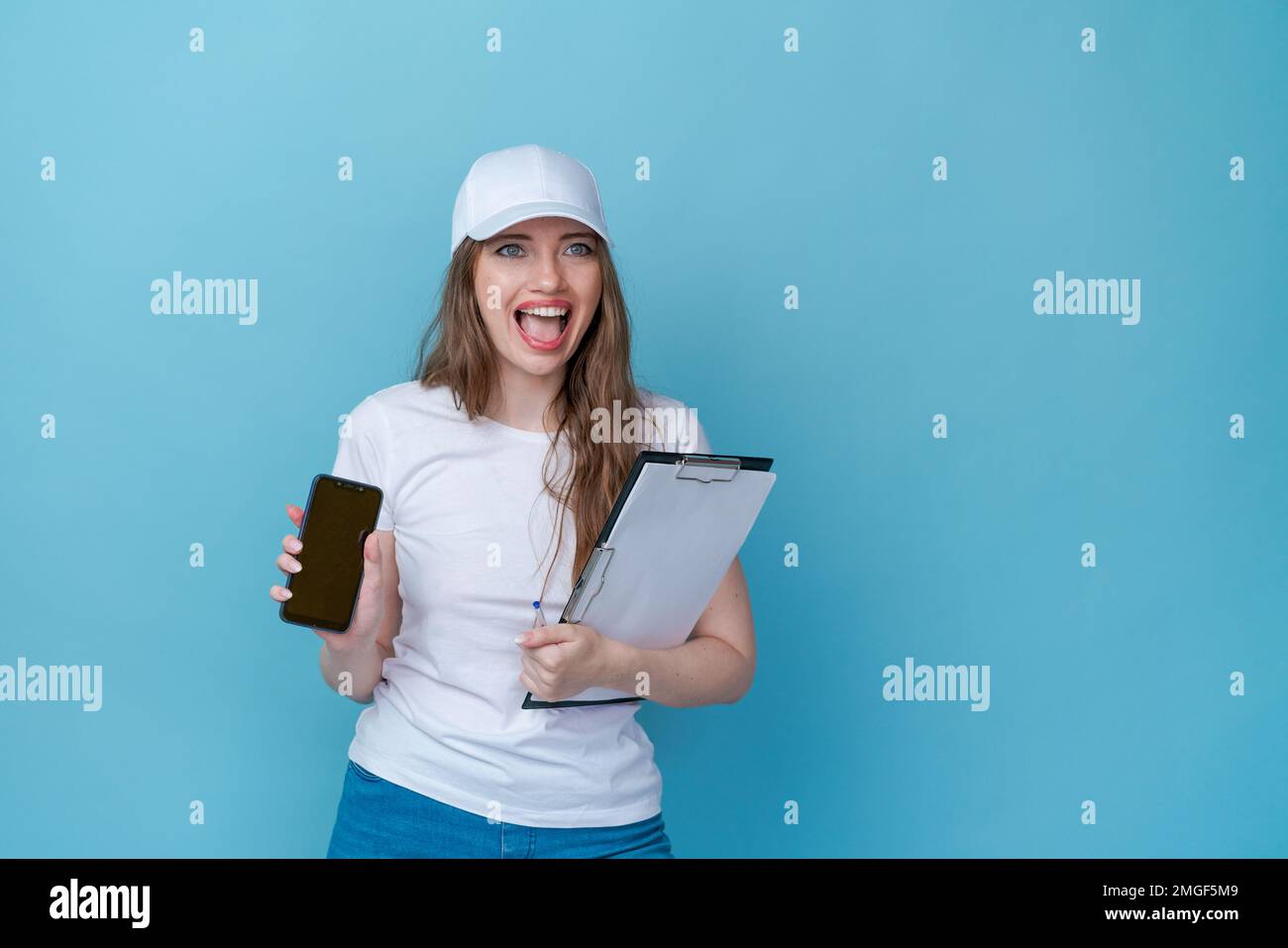 Call center service concept customer support or sales agent. Business woman, caller, telephone operator consultant, holding survey papers in white t-shirt and cap for mockup on blue studio background Stock Photo