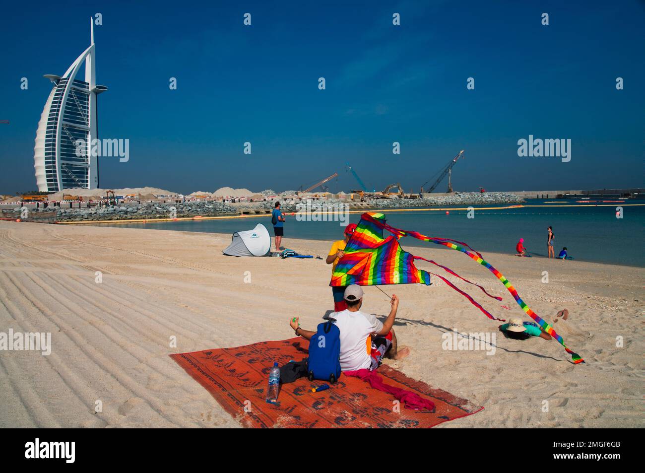 A young boy prepares to fly a kite on a public beach with the Burj al