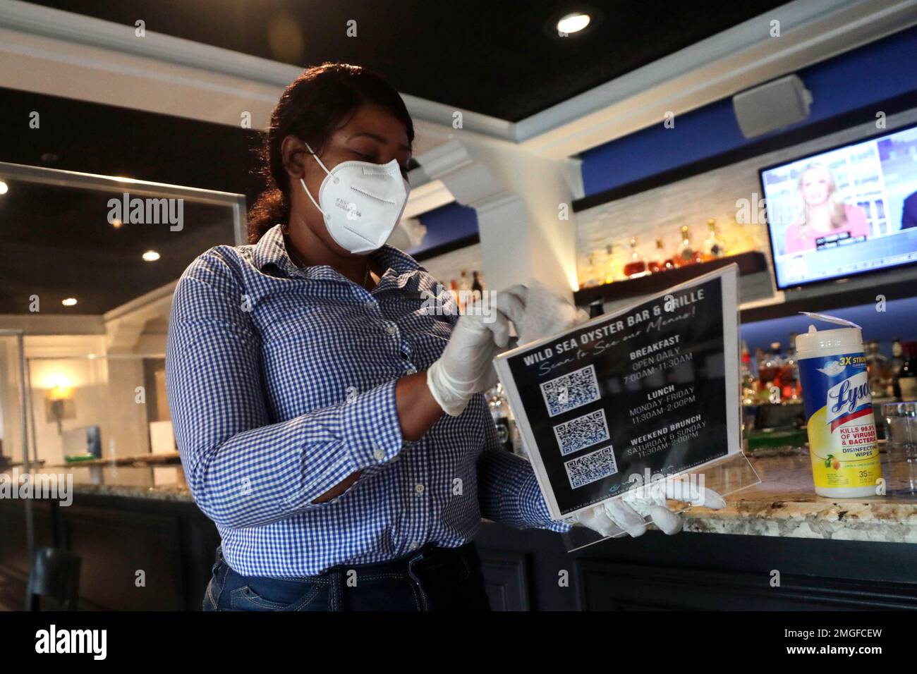 Judith Bazile wears a protective mask and gloves as she cleans an  electronic menu at the Wild Sea Oyster Bar and Grille at the Riverside  Hotel during the new coronavirus pandemic, Tuesday,