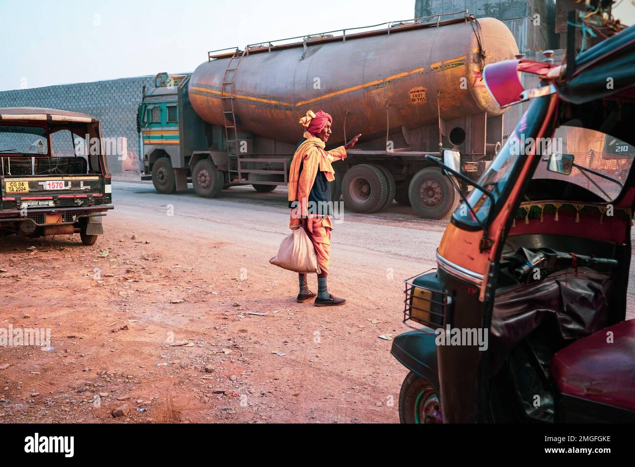 Old Indian man wearing a red turban and orange dhoti kurta with jacket standing and waiting for transport vehicle on main road, An old man standing on Stock Photo
